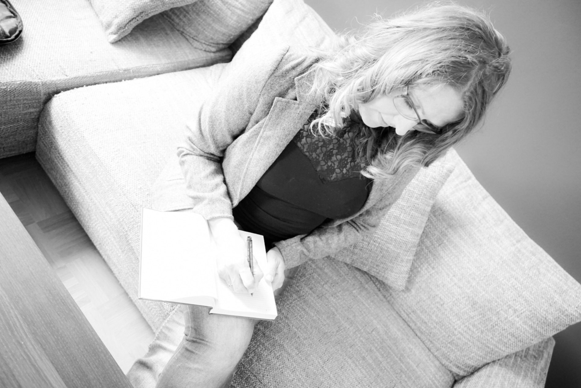 Ordnungshexe Janine Rempel sitzt auf dem Sofa und schreibt inn ein Buch, schwarzweiß Bild